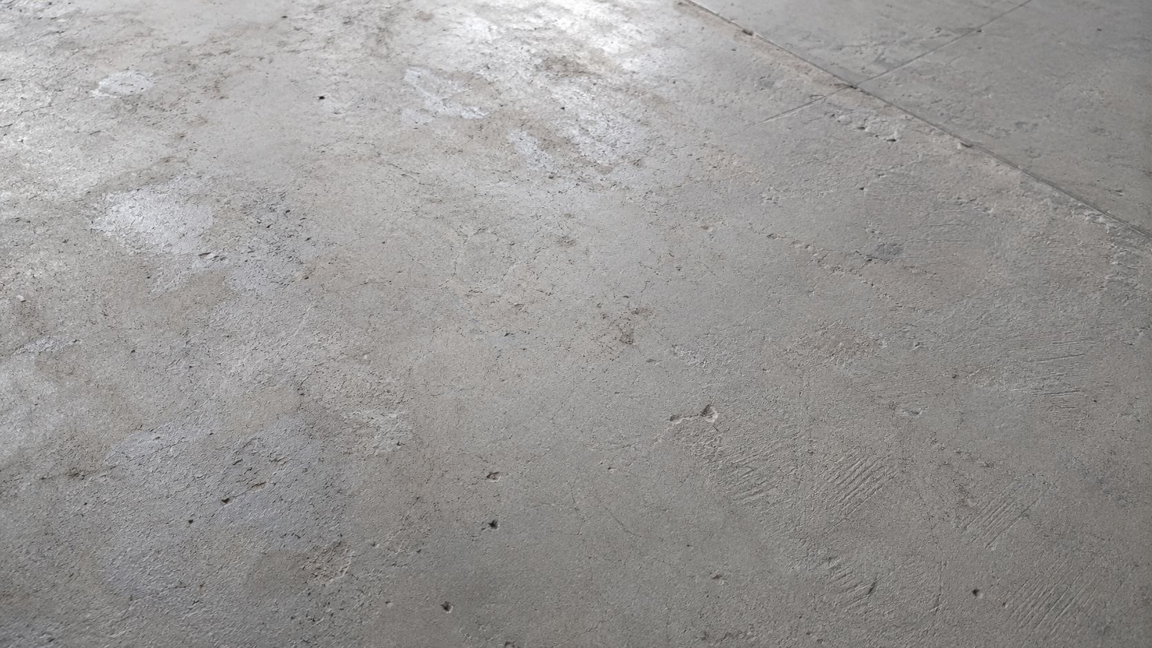 En tekstur af en rå betonoverflade med tydelige spor af slid, ridser og ujævnheder i grå nuancer.